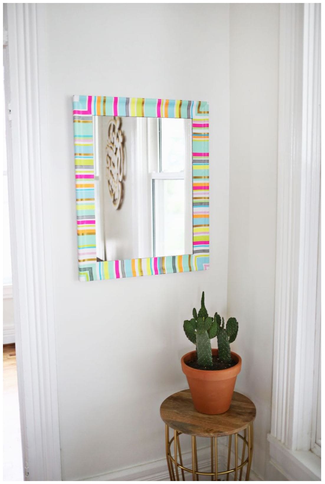 A white mirror decorated with colorful strips of washi tape hanging on a white wall.