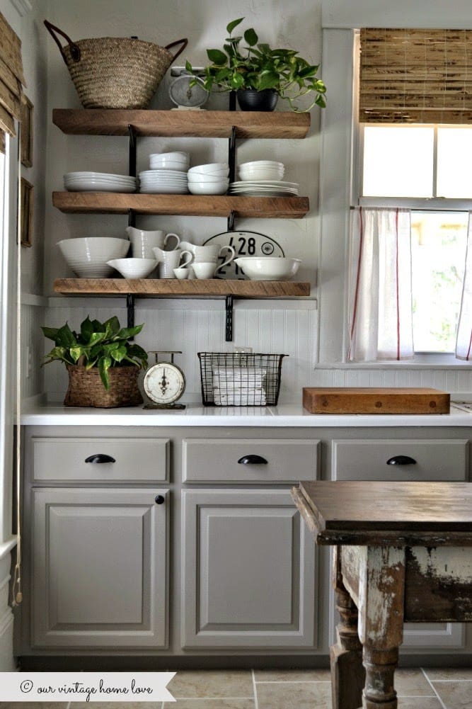 A farmhouse style kitchen with gray cabinets, open shelving, and white dishes.