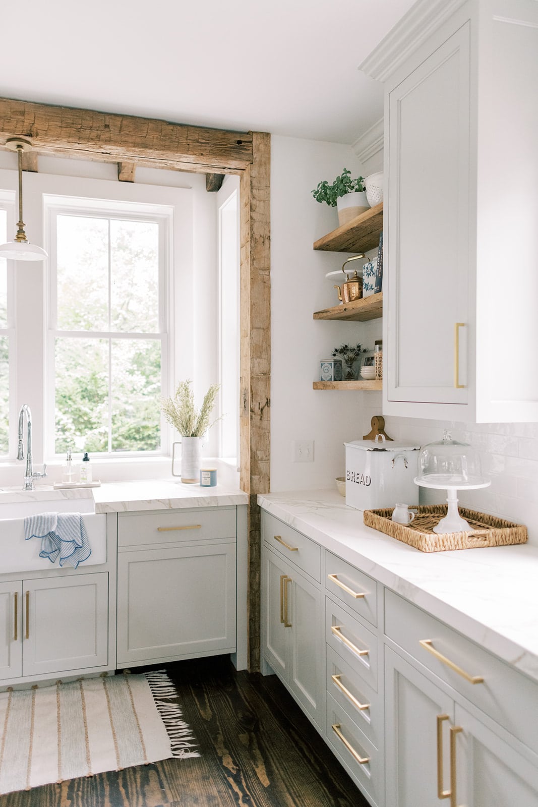 A farmhouse sink surrounded by gray cabinets and reclaimed barnwood beams.