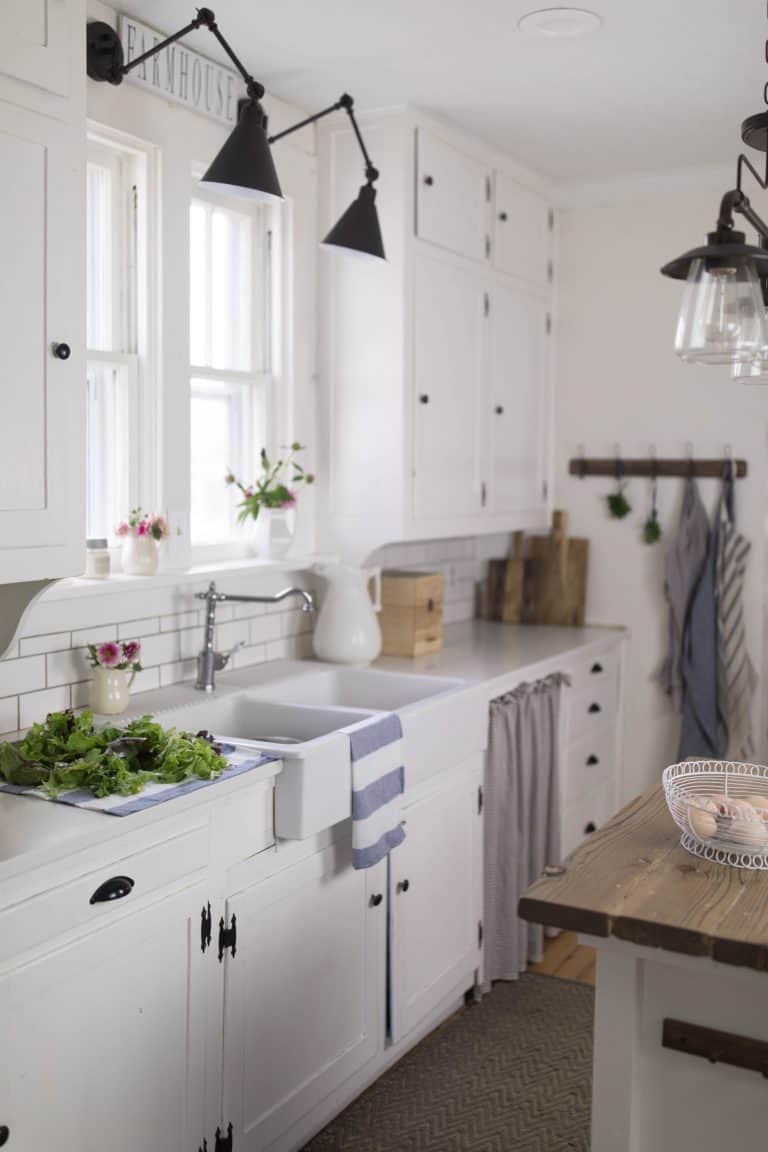 A white farmhouse style kitchen with summer flowers in white pitchers.