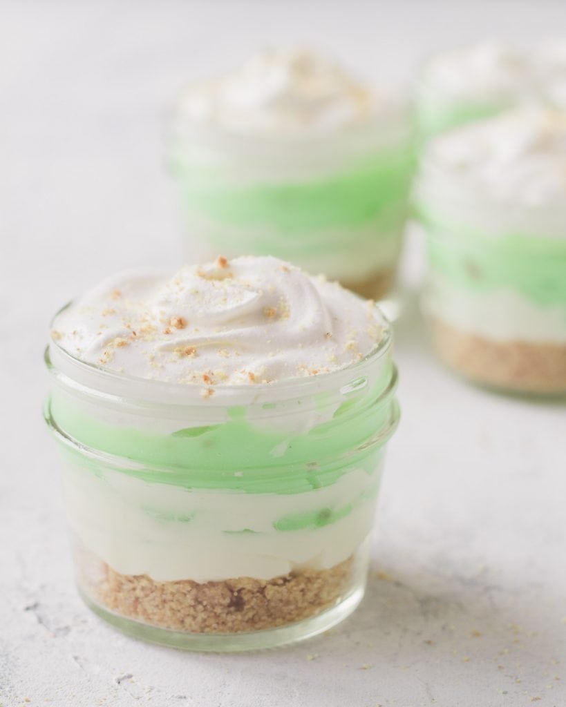 A mini dessert-in-jar layered with crust, cream cheese filling, pistachio pudding, and frozen whipped topping.