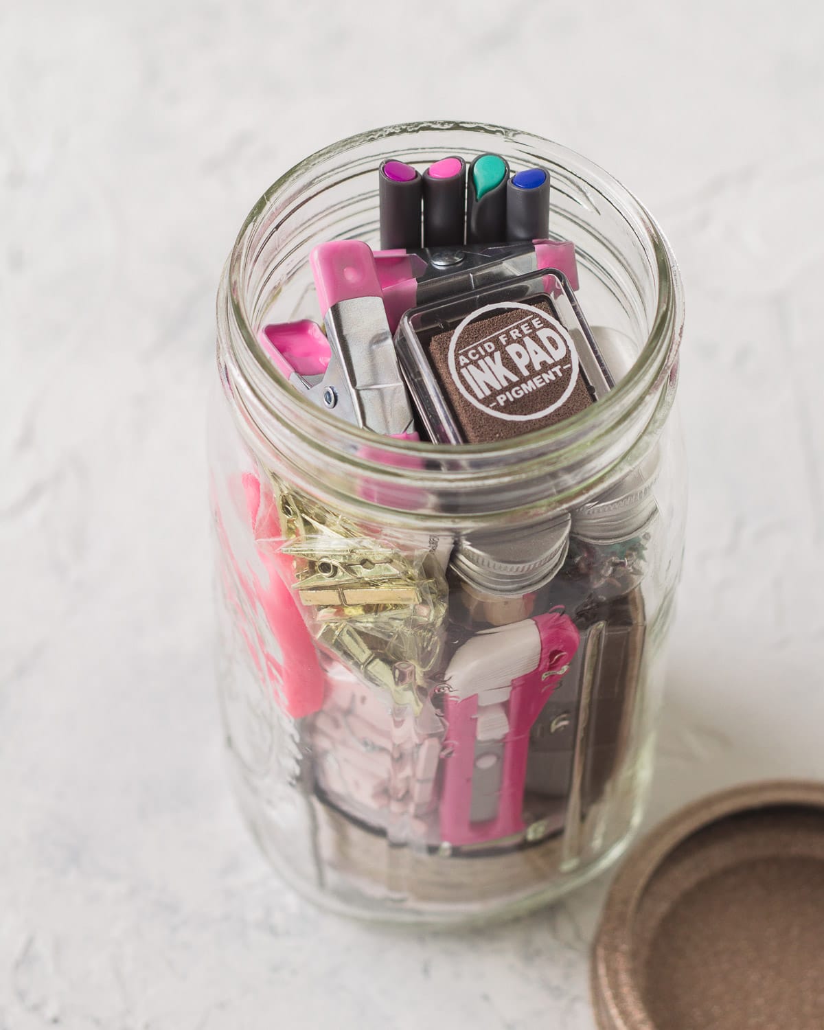 A mason jar gift filled with various craft supplies like rubber stamps and ink.