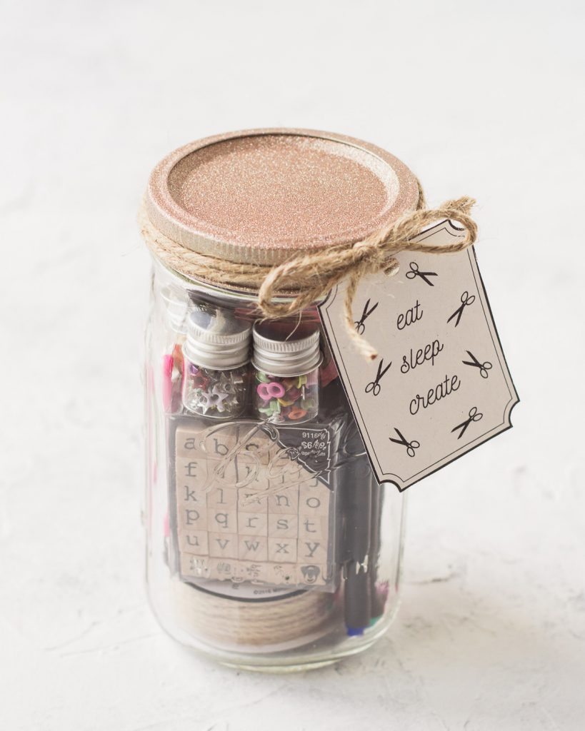 A mason jar gift filled with craft supplies and tied with a handmade gift tag.
