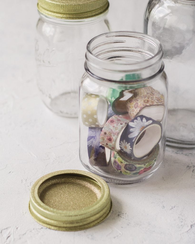 A glittery gold mason jar lid and a jar full of floral washi tape.