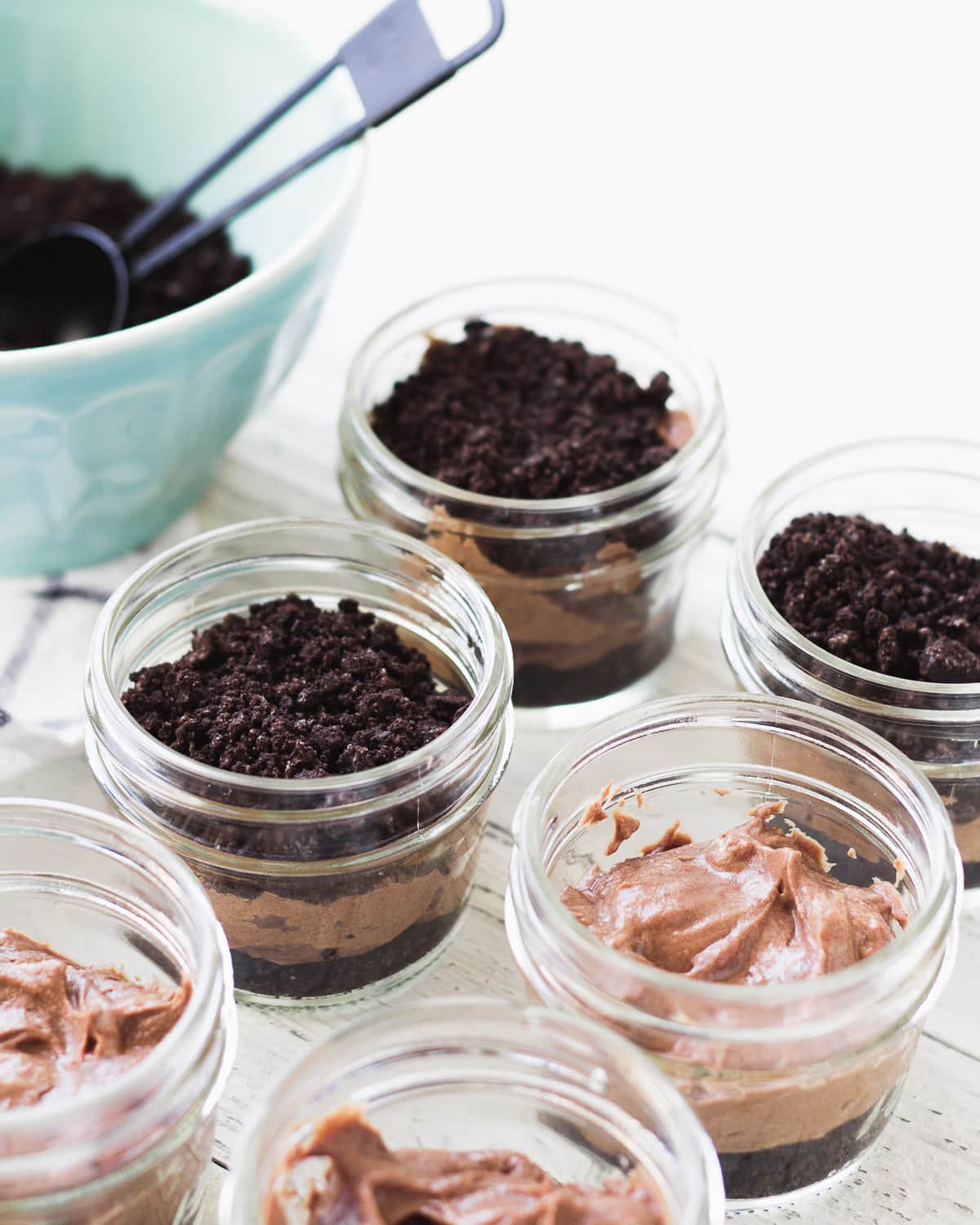 Layering oreo cookie crumbs and chocolate filling into dessert jars.