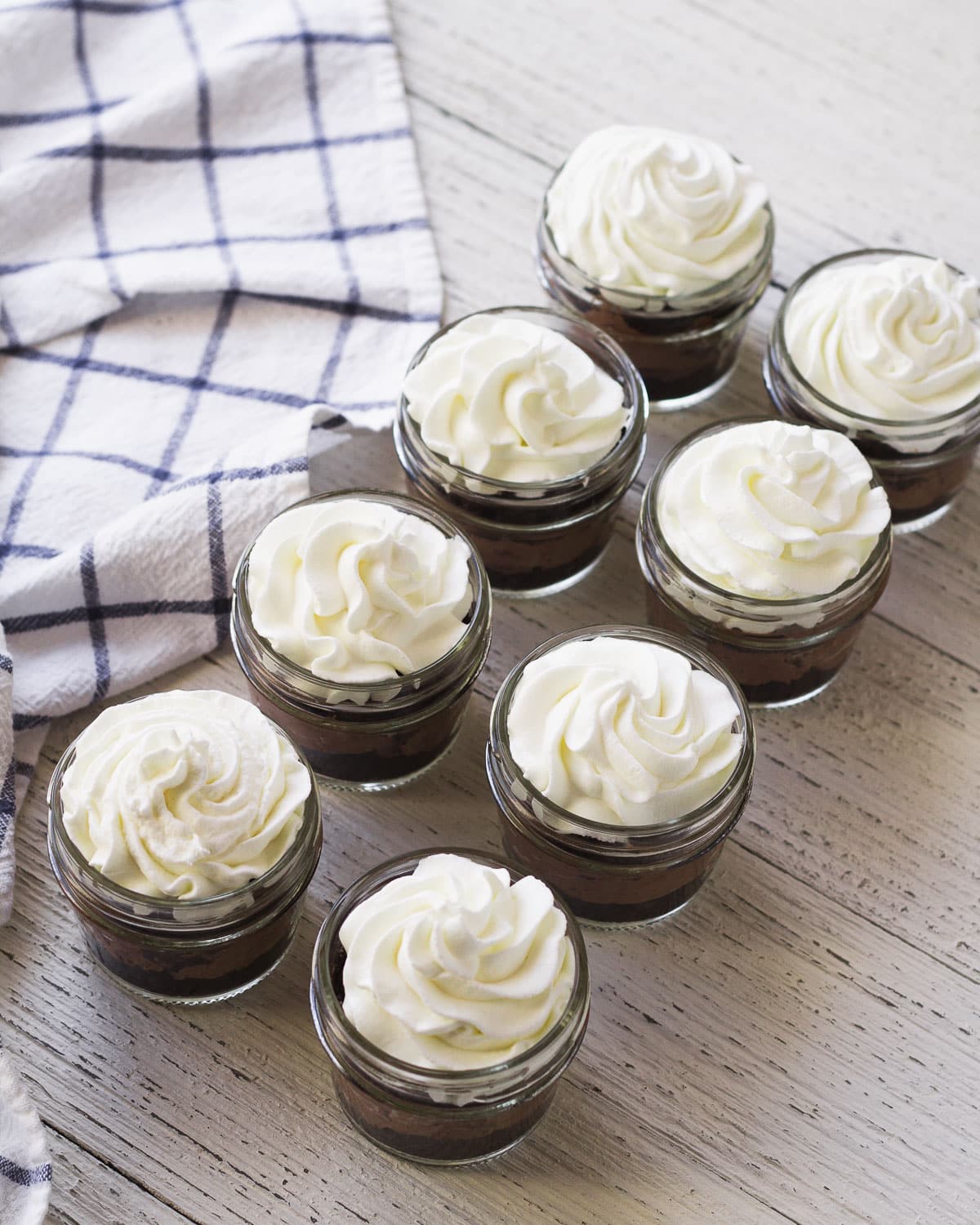 Eight mason jars filled with chocolate layers and topped with whipped cream.