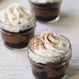 A mini chocolate mason jar dessert topped with whipped cream and a sprinkle of cocoa powder.