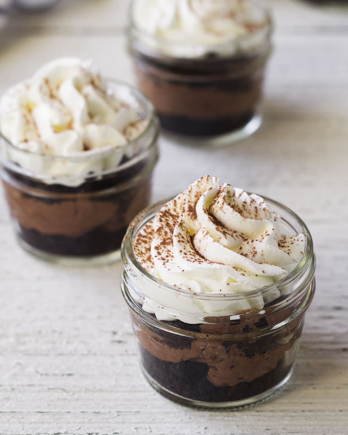 A mini chocolate mason jar dessert topped with whipped cream and a sprinkle of cocoa powder.