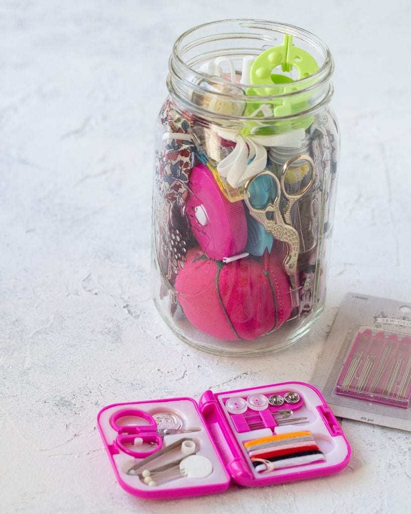 A miniature sewing kit in front of a larger mason jar sewing kit.