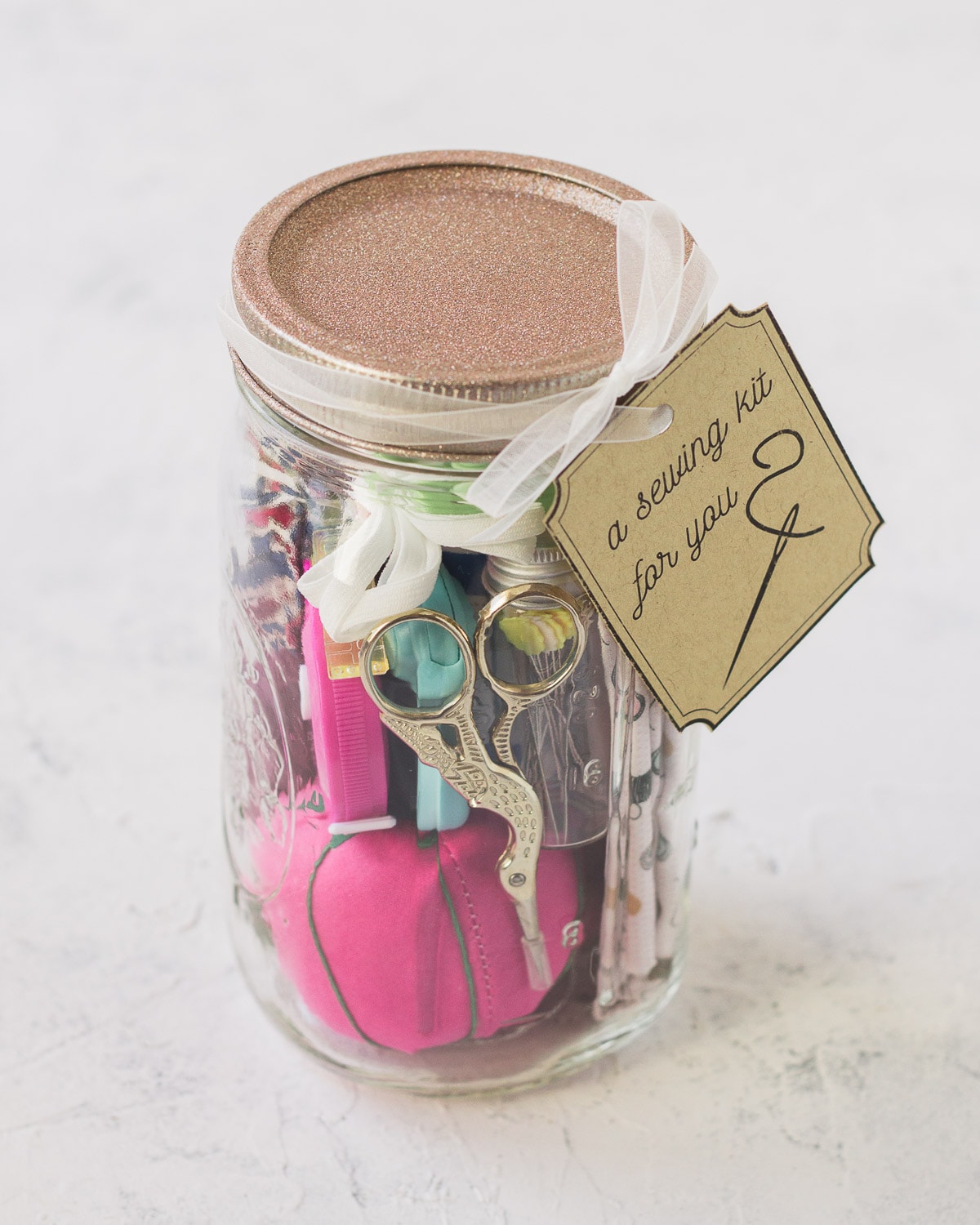 A sewing kit mason jar filled with a pincushion, embroidery scissors, fabric, and more.