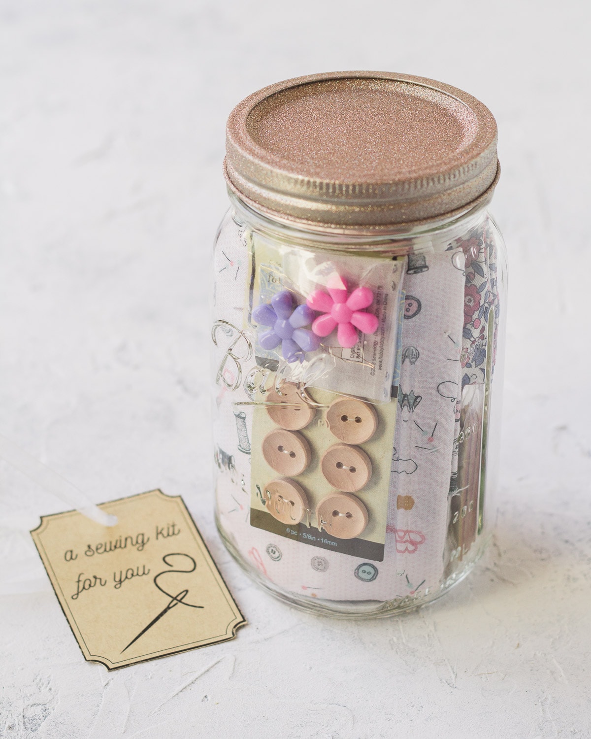 A mason jar sewing kit filled with buttons, fabric, and more.