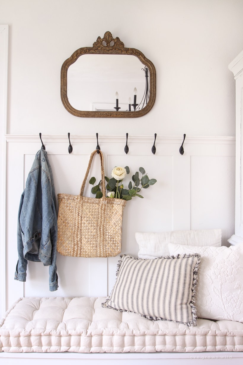 Entryway with white walls, and mirror, and black coat hooks.