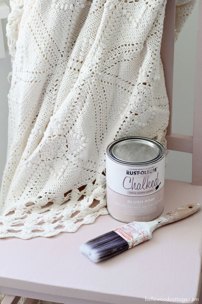 A pink chalk painted chair with a can of paint and brush on top.