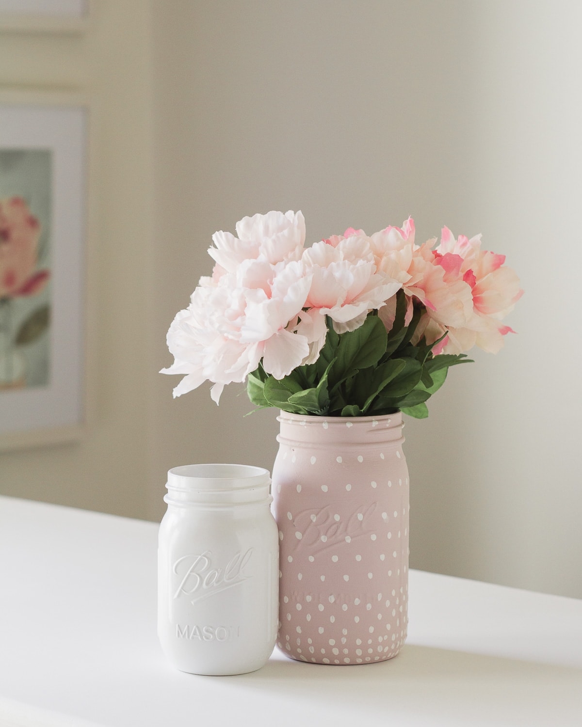 A white painted mason jar and a pink (with white polka dots) mason jar with flowers inside.