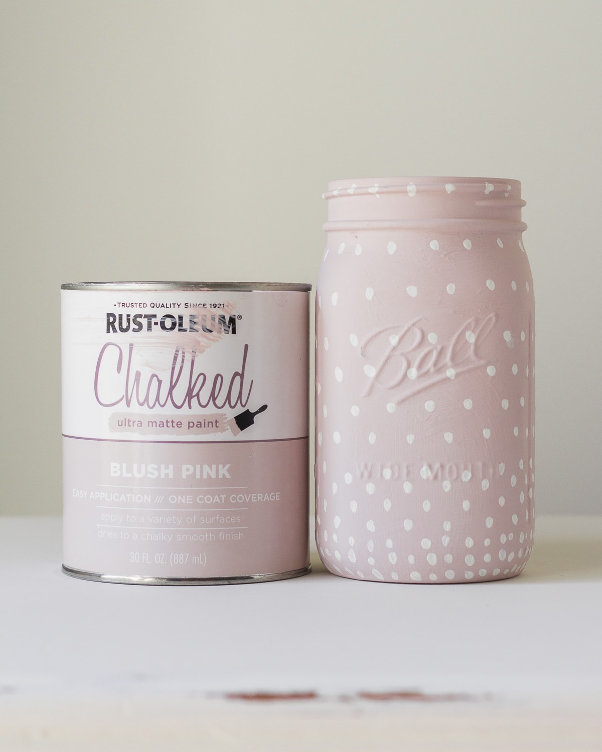 A can of Rust-Oleum chalked paint in Blush Pink and a glass jar painted with the paint, plus white polka dots.