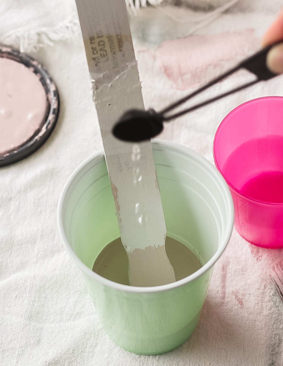 Using a teaspoon to add water to a cup of chalk paint to thin it down.