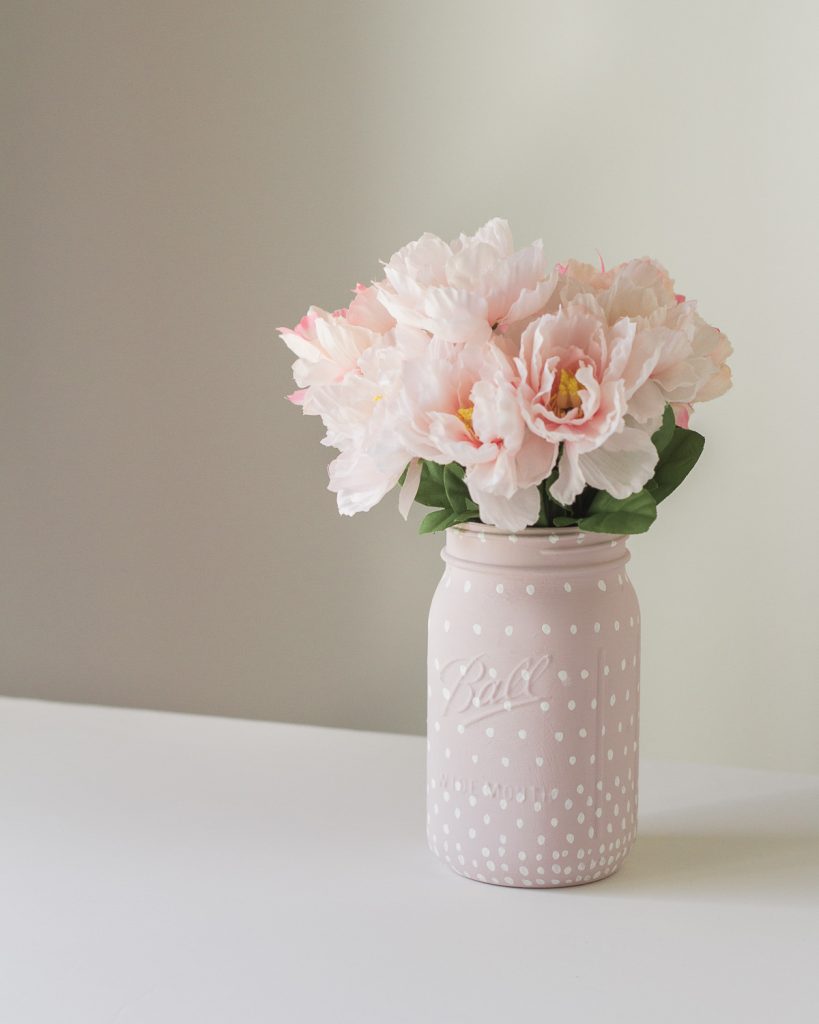 A painted glass jar filled with pink faux flowers.