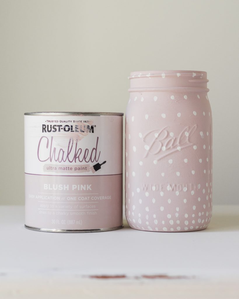A can of chalk paint and a glass jar painted pink with white polka dots.
