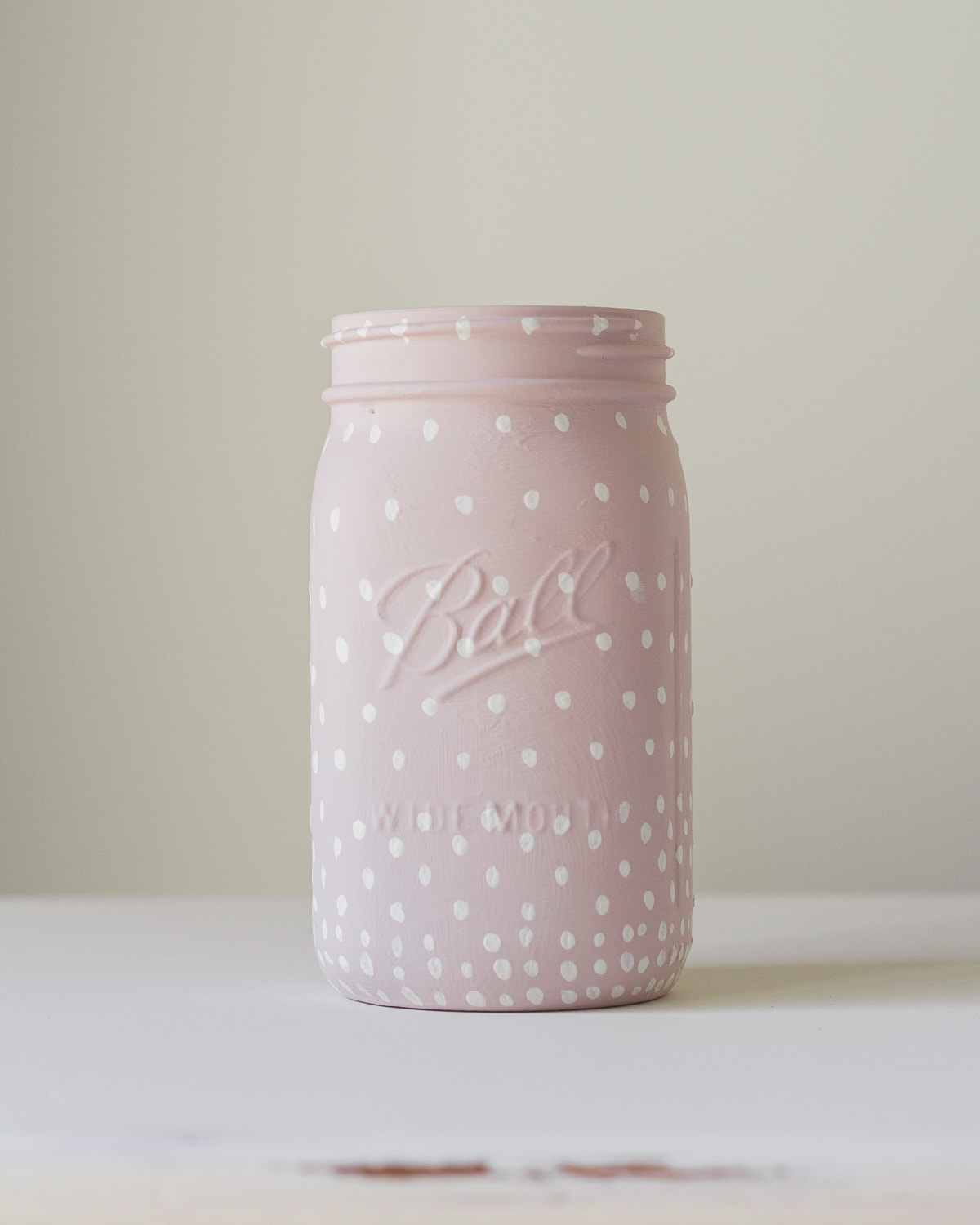 A ball mason jar painted pink with white polka dots.