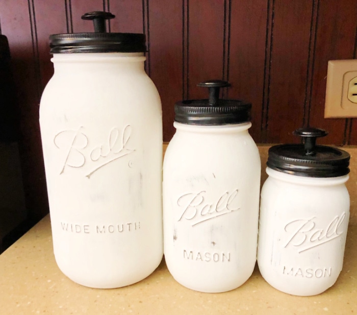 Three mason jars painted white and turned into canisters with the addition of knobs to the lids.