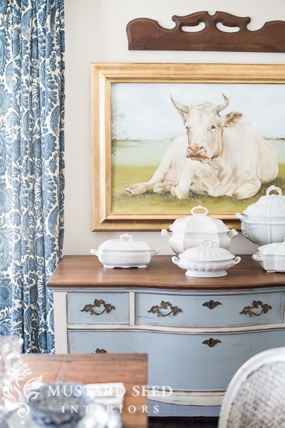 A painting of a cow and a blue dresser.