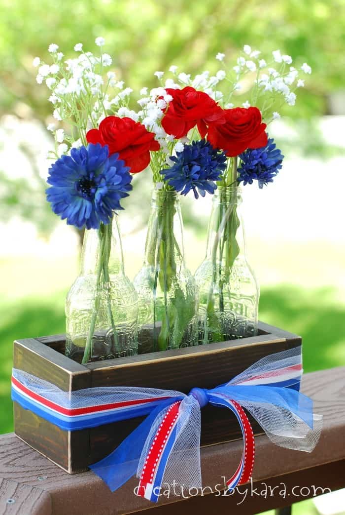 A red, white, and blue centerpiece with three glass bottles filled with red, white, and blue flowers.
