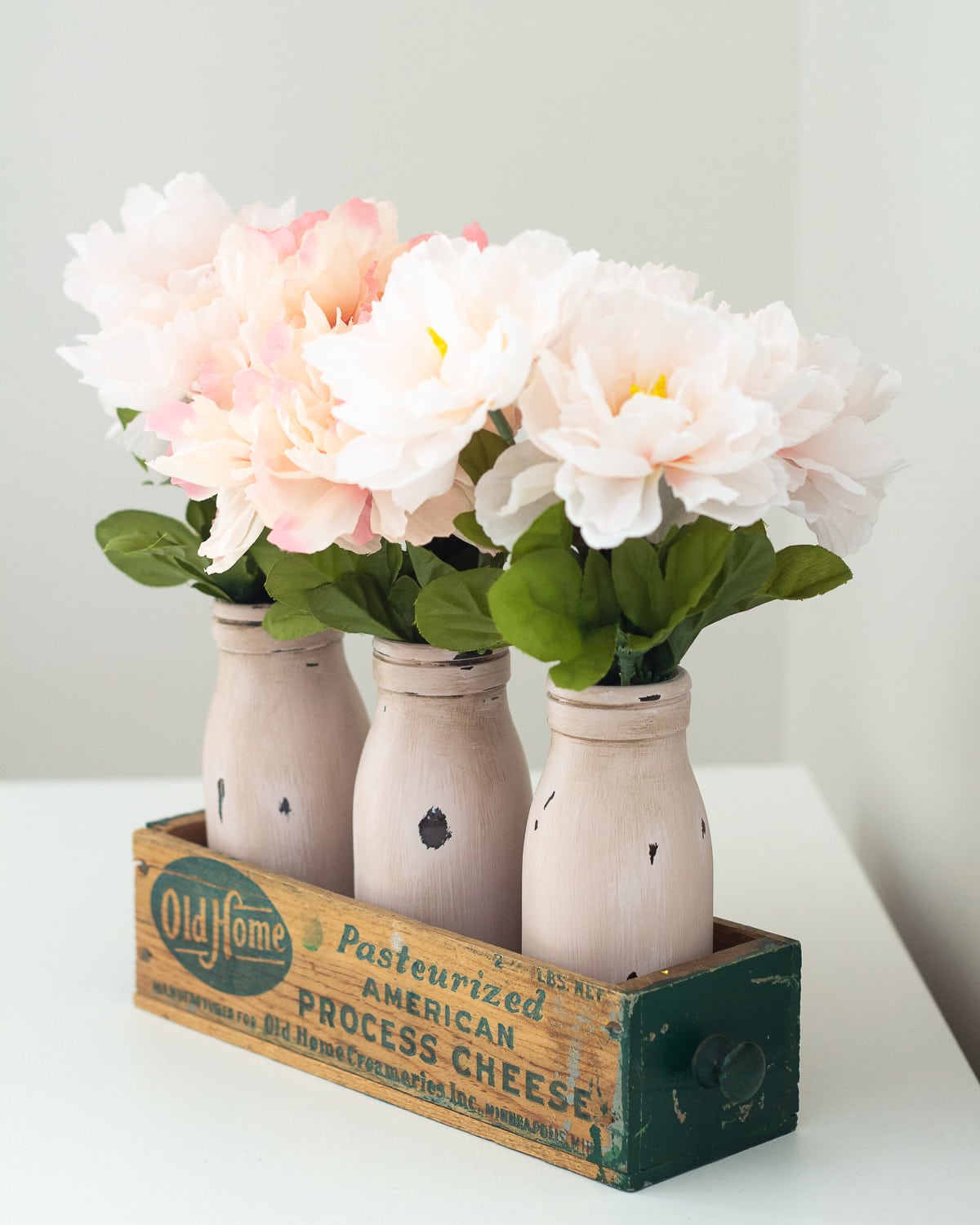 Chalk painted and distressed milk bottles in a vintage cheese box.