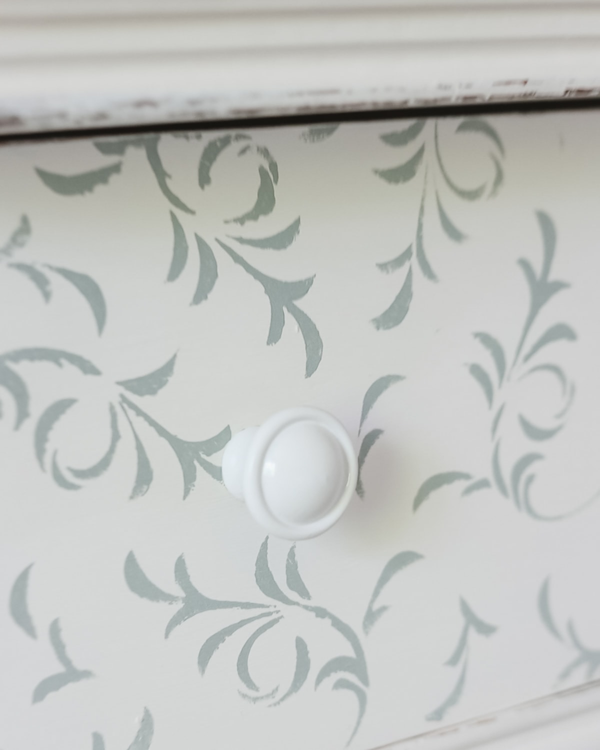 A close-up look at a knob spray-painted white and installed on a stenciled dresser.