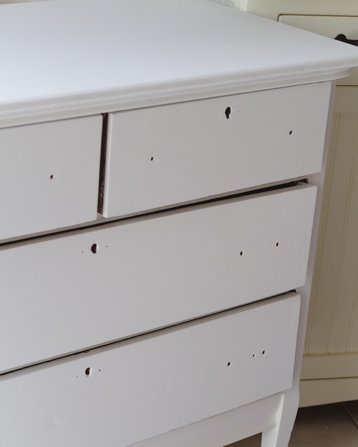 A vintage dresser painted white with the hardware removed.