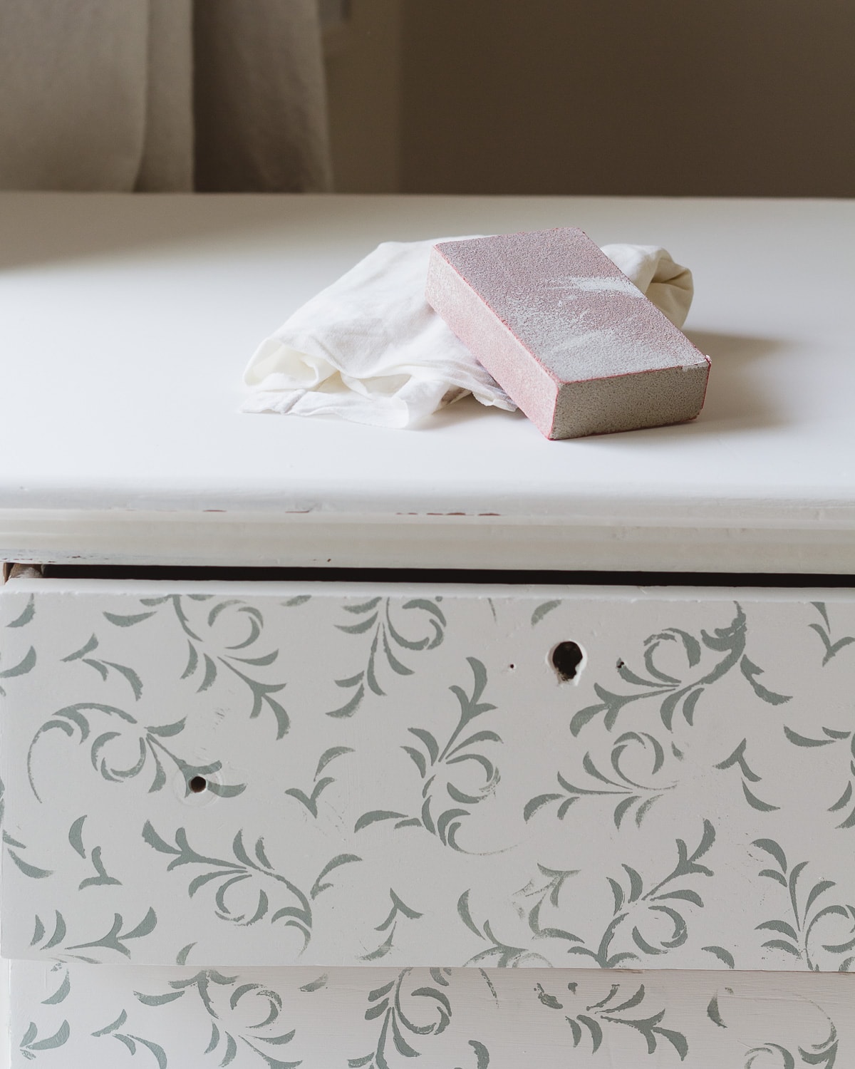 A sanding block on top of stenciled dresser.