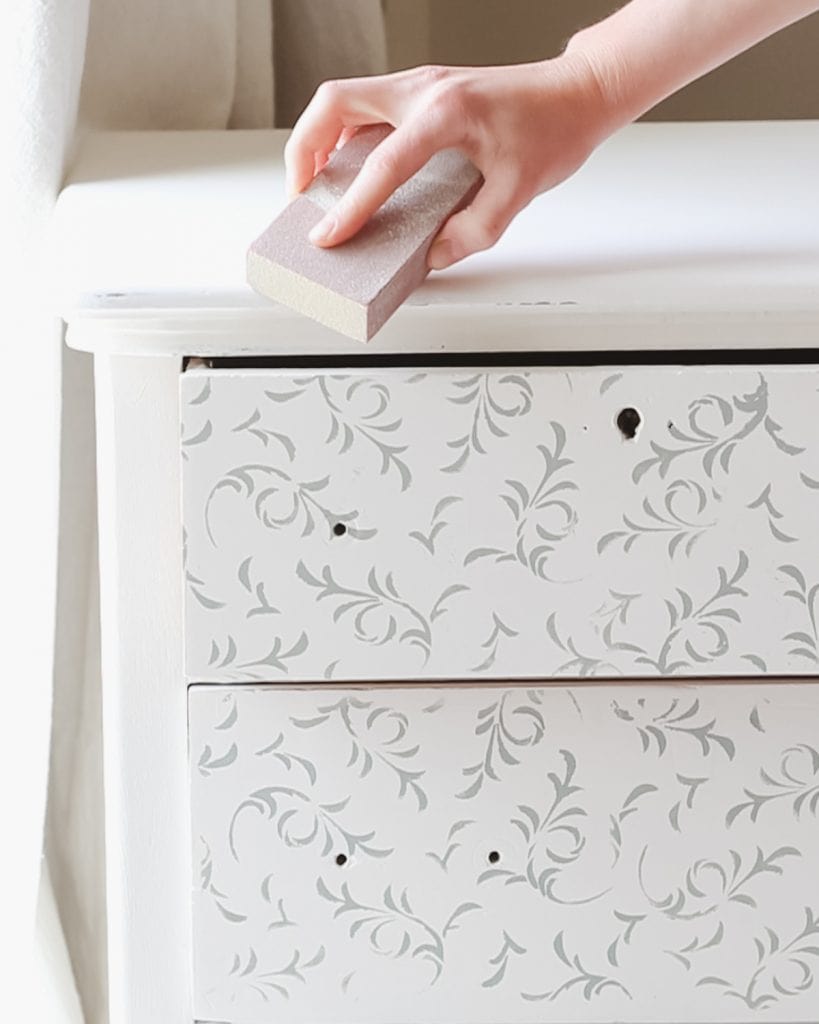 Distressing a painted dresser with a sanding block.