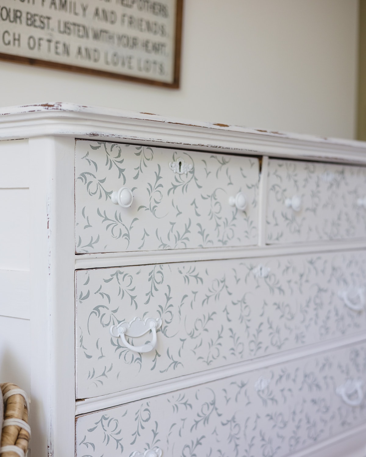 A vintage dresser painted white with blue floral stenciling and spray-painted white hardware.