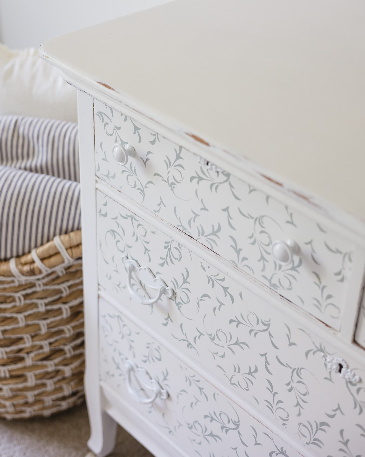 A vintage white dresser with stenciled blue florals and white hardware.