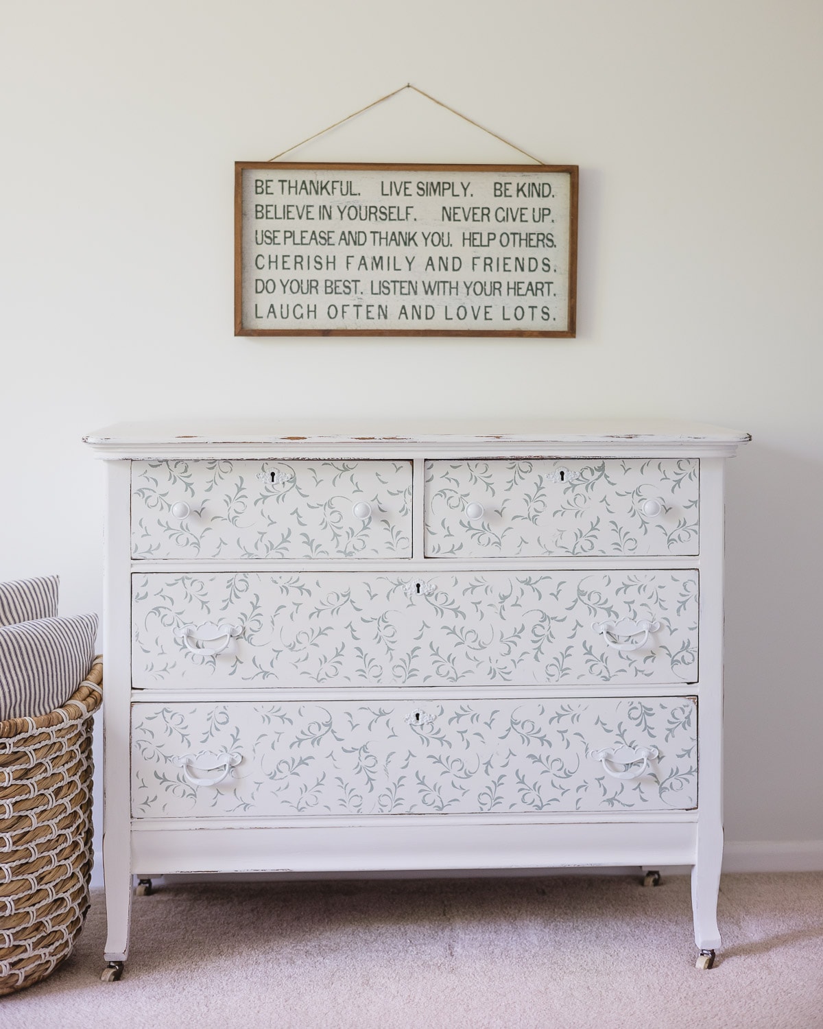 A stenciled white and blue dresser with inspirational farmhouse wall art hanging above it.