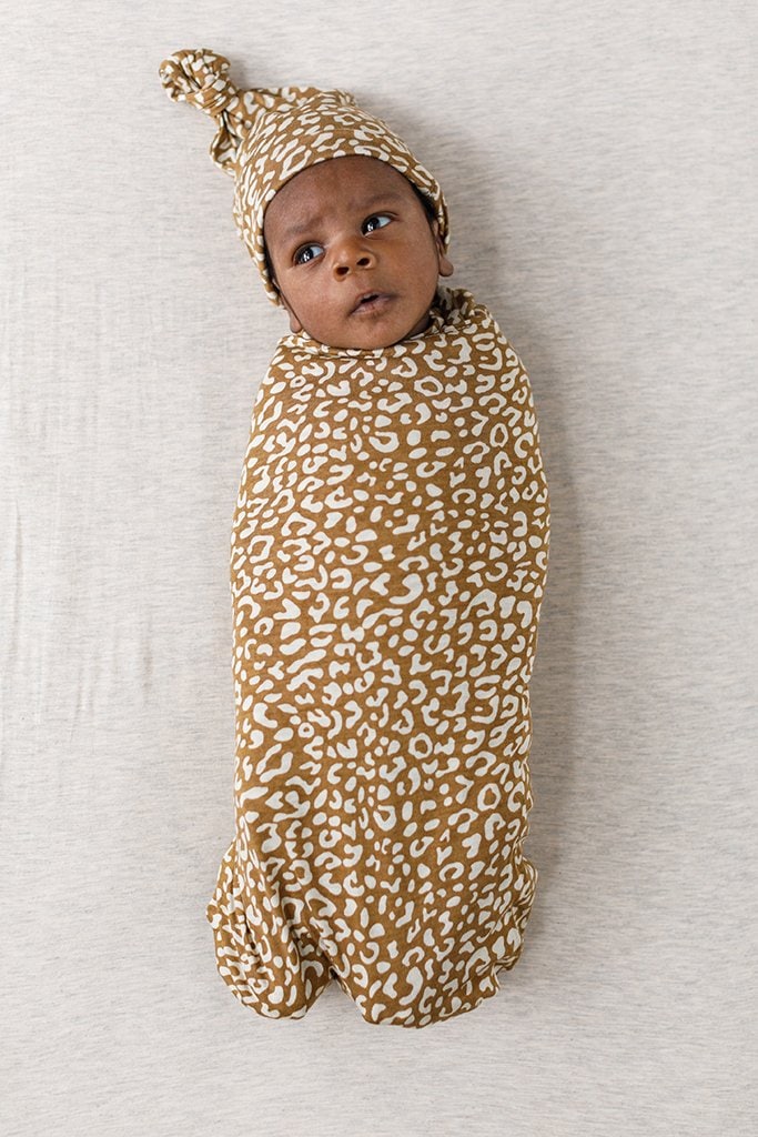 A baby wrapped in a leopard print swaddle with matching hat.