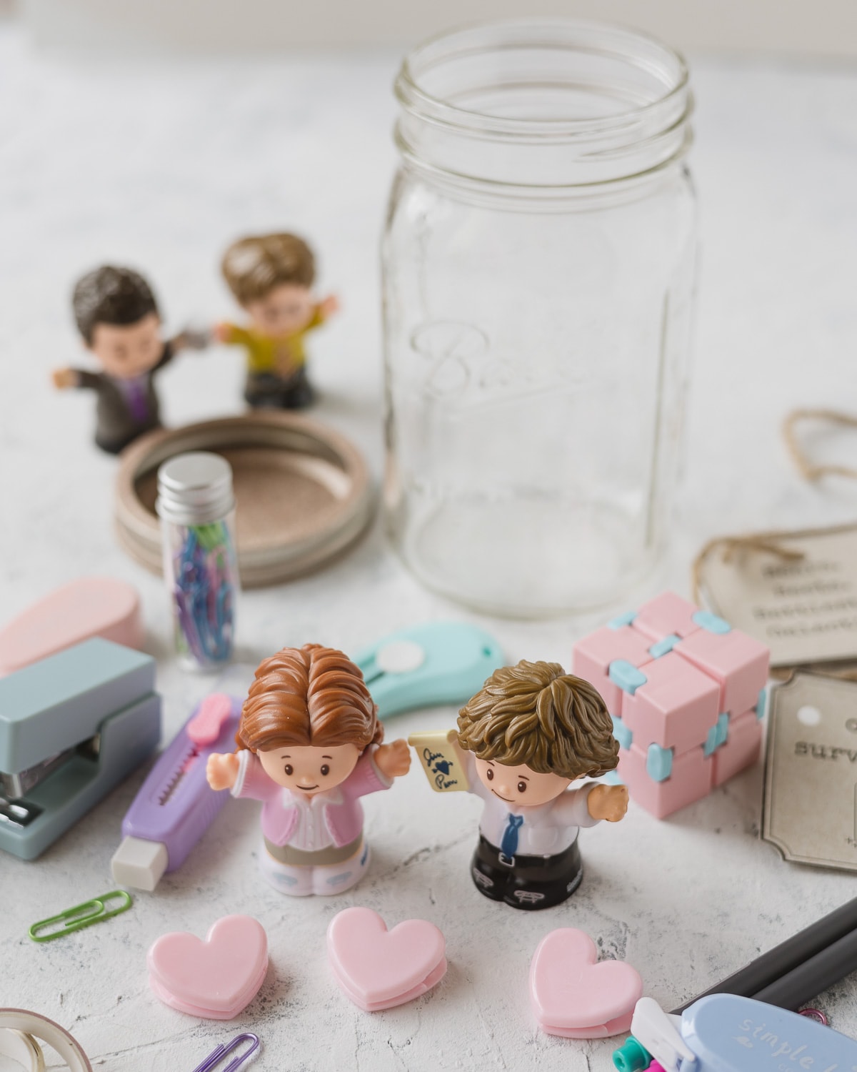 Fisher Price Little People "Jim" and "Pam" from The Office surrounded by office supplies.