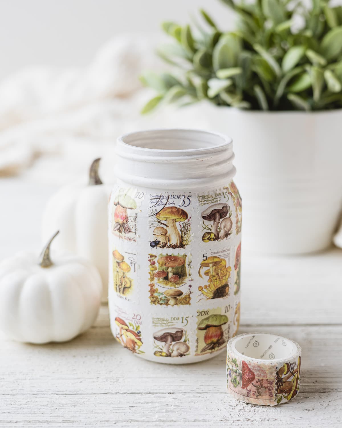 A mason jar painted white and covered with postage stamp washi tape.