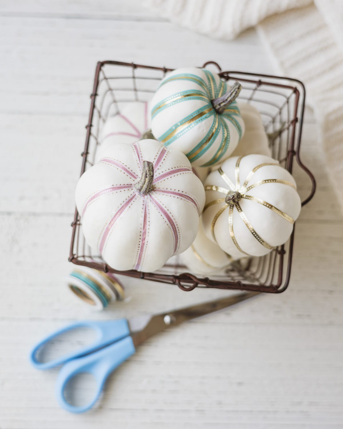 White foam pumpkins decorated with colorful washi tape and arranged in a metal basket.