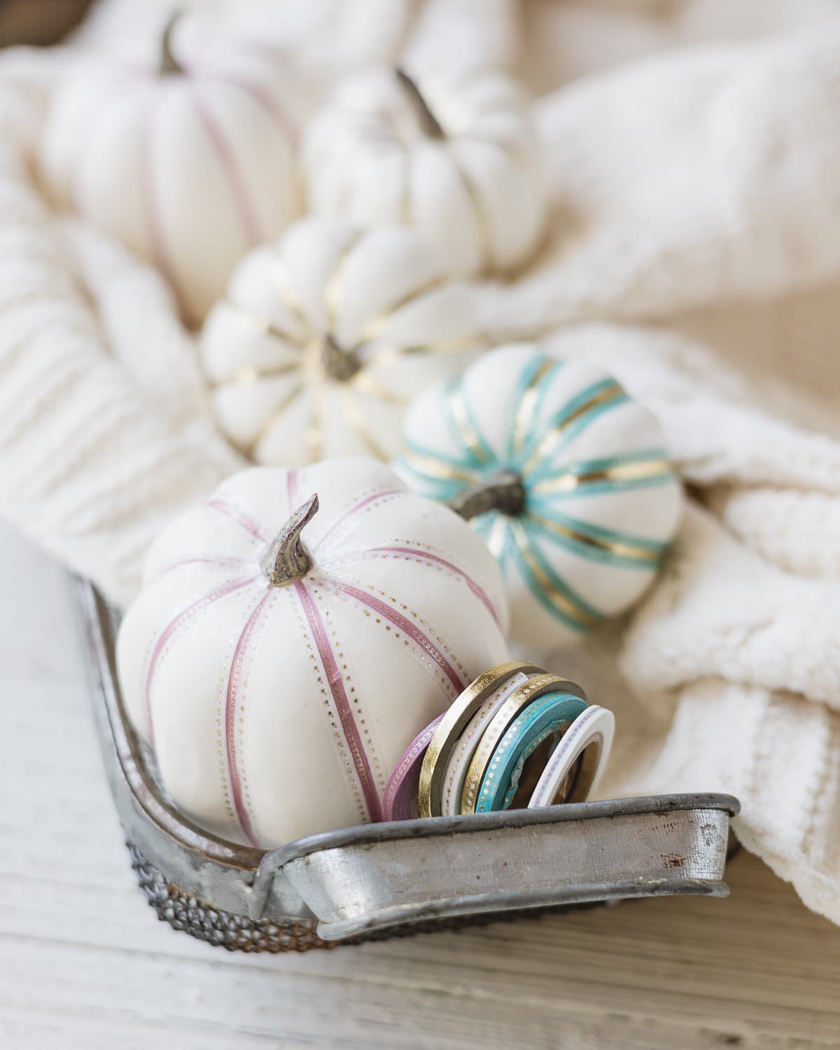 White faux pumpkins decorated with thin washi tape and arranged in a metal basket.