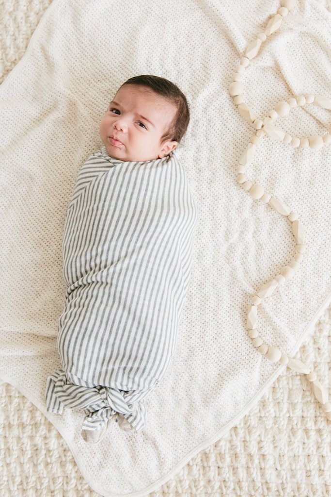 A baby wrapped in a striped stretchy swaddle blanket.