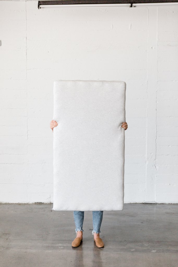 A person holding up a crib mattress with a Solly Baby sheet on it.