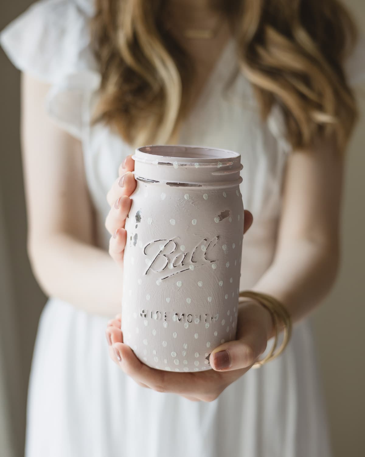 A woman holding a mason jar painted with light pink chalk paint.