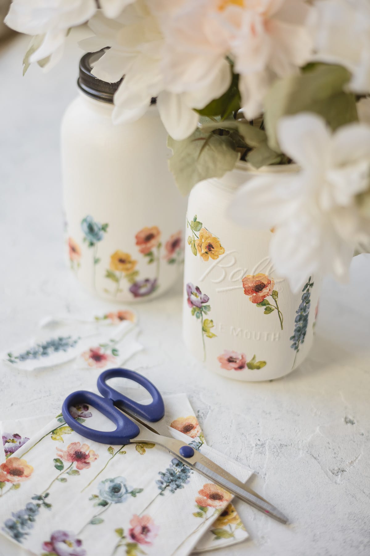 Floral mason jar centerpieces, floral paper napkins, and a pair of small scissors.