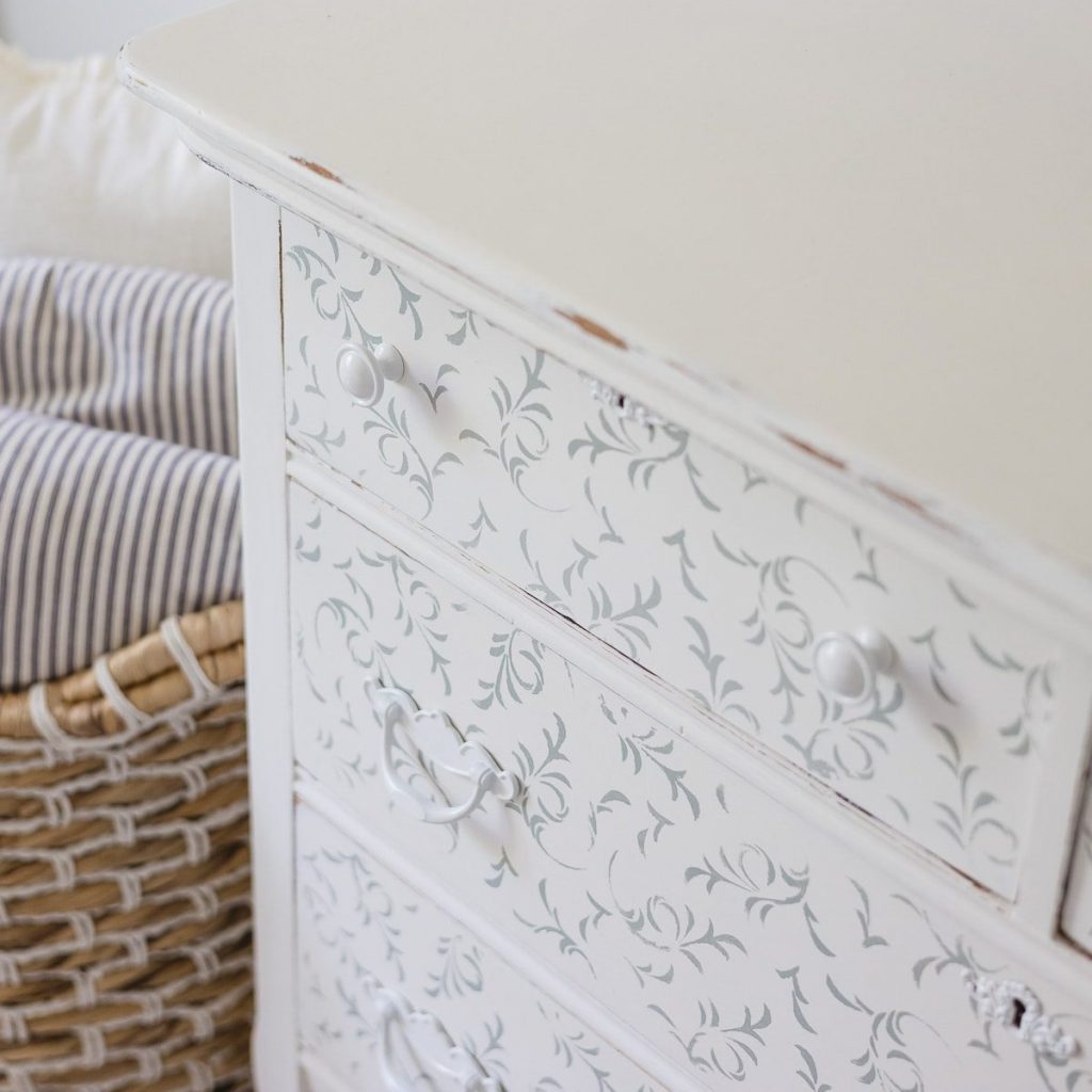 A vintage white dresser with stenciled blue florals and white hardware.