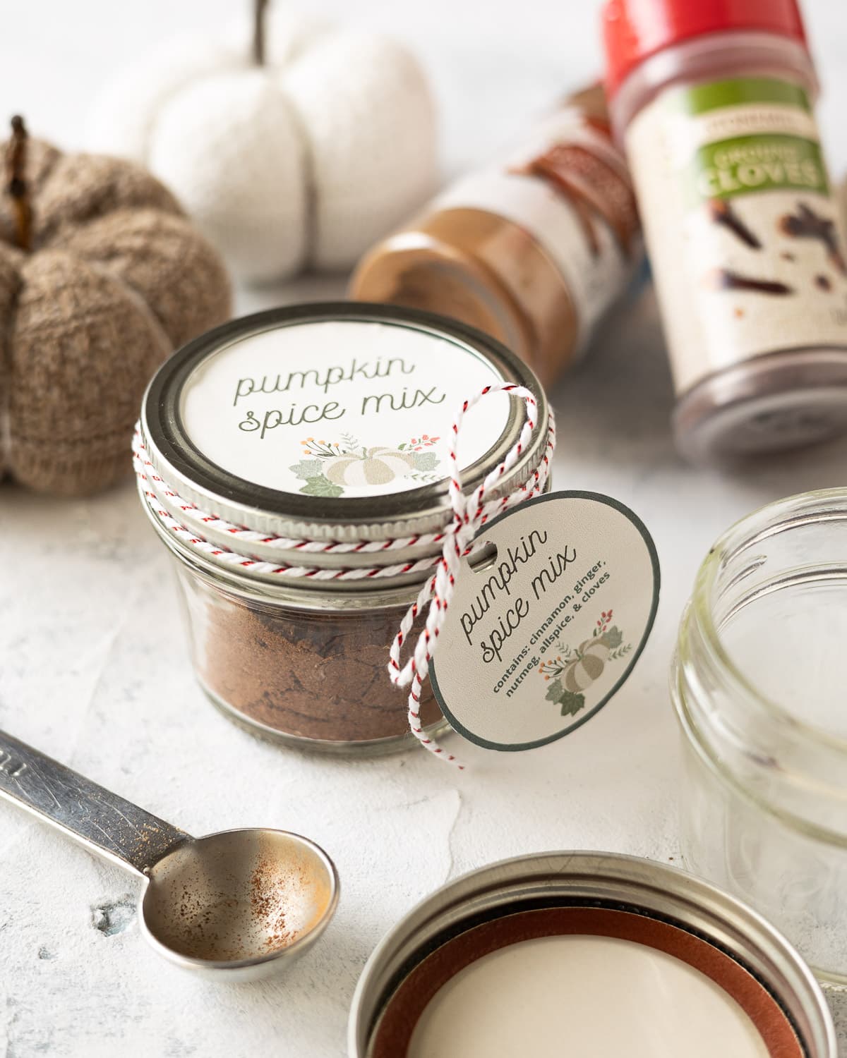 A jar of homemade pumpkin spice mix surrounded by spice jars and a measuring spoon.