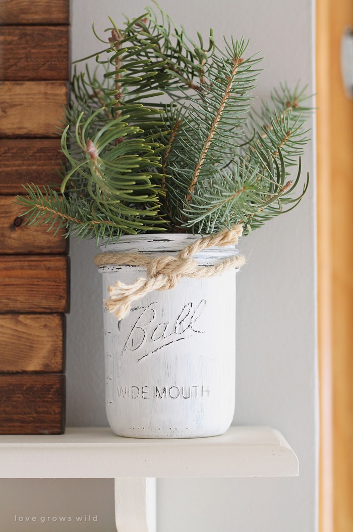 A painted and distressed mason jar with evergreen branches inside.