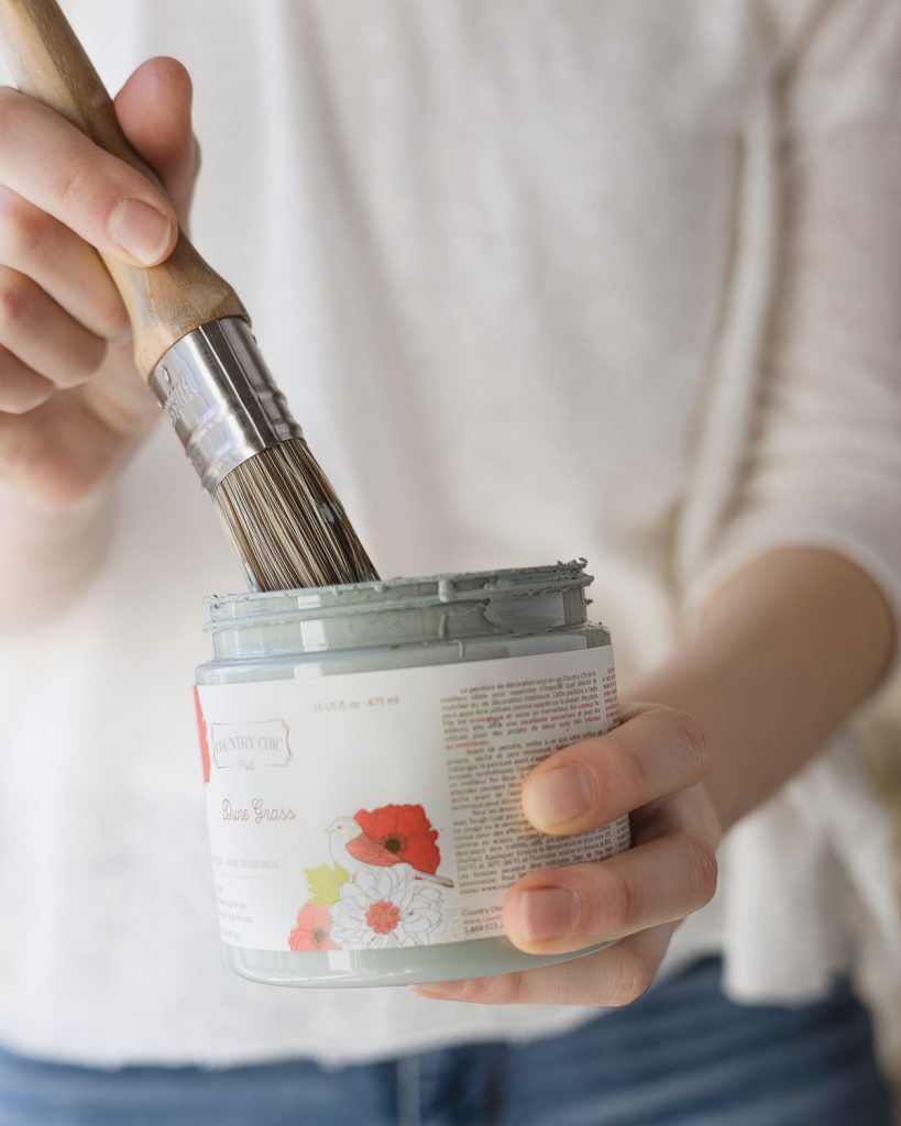 A paintbrush dipping into a container of light blue-green paint.