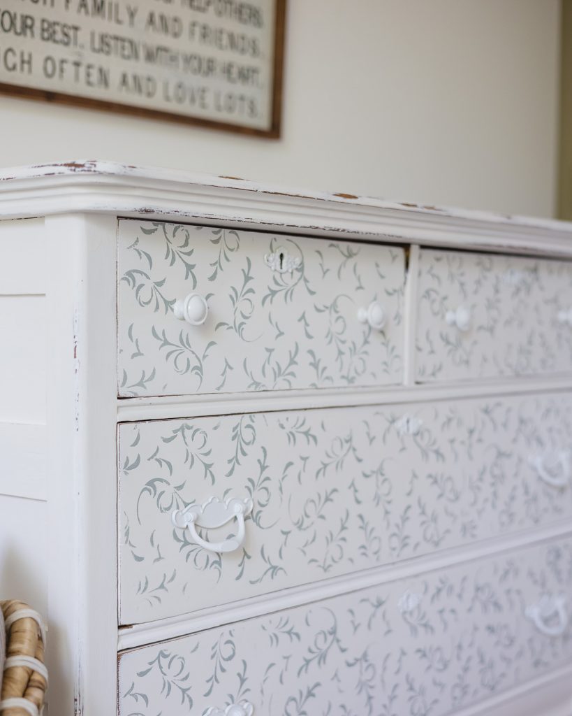 A dresser painted white with light blue stenciling.