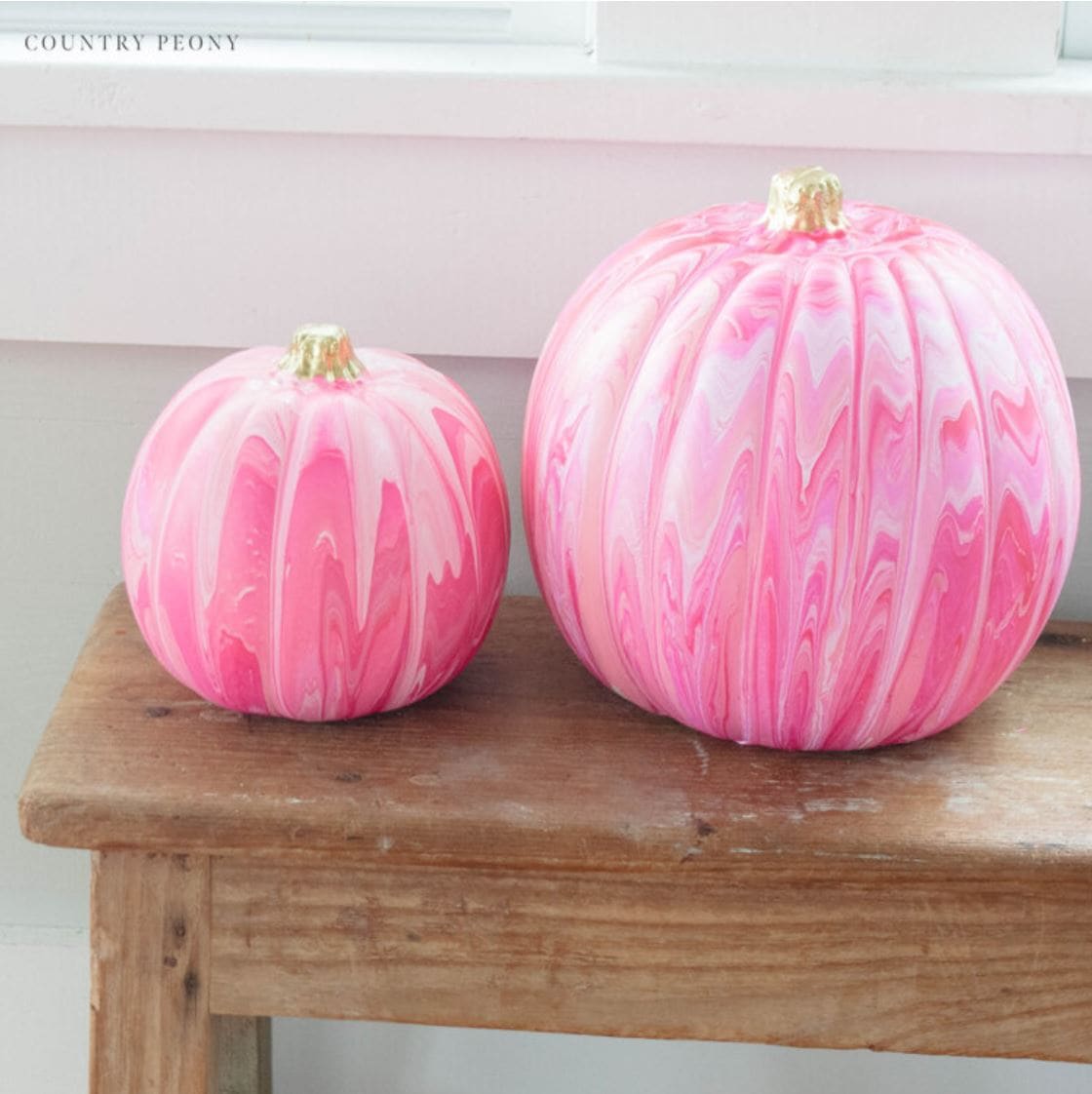 Two pink paint poured pumpkins on a wooden bench.