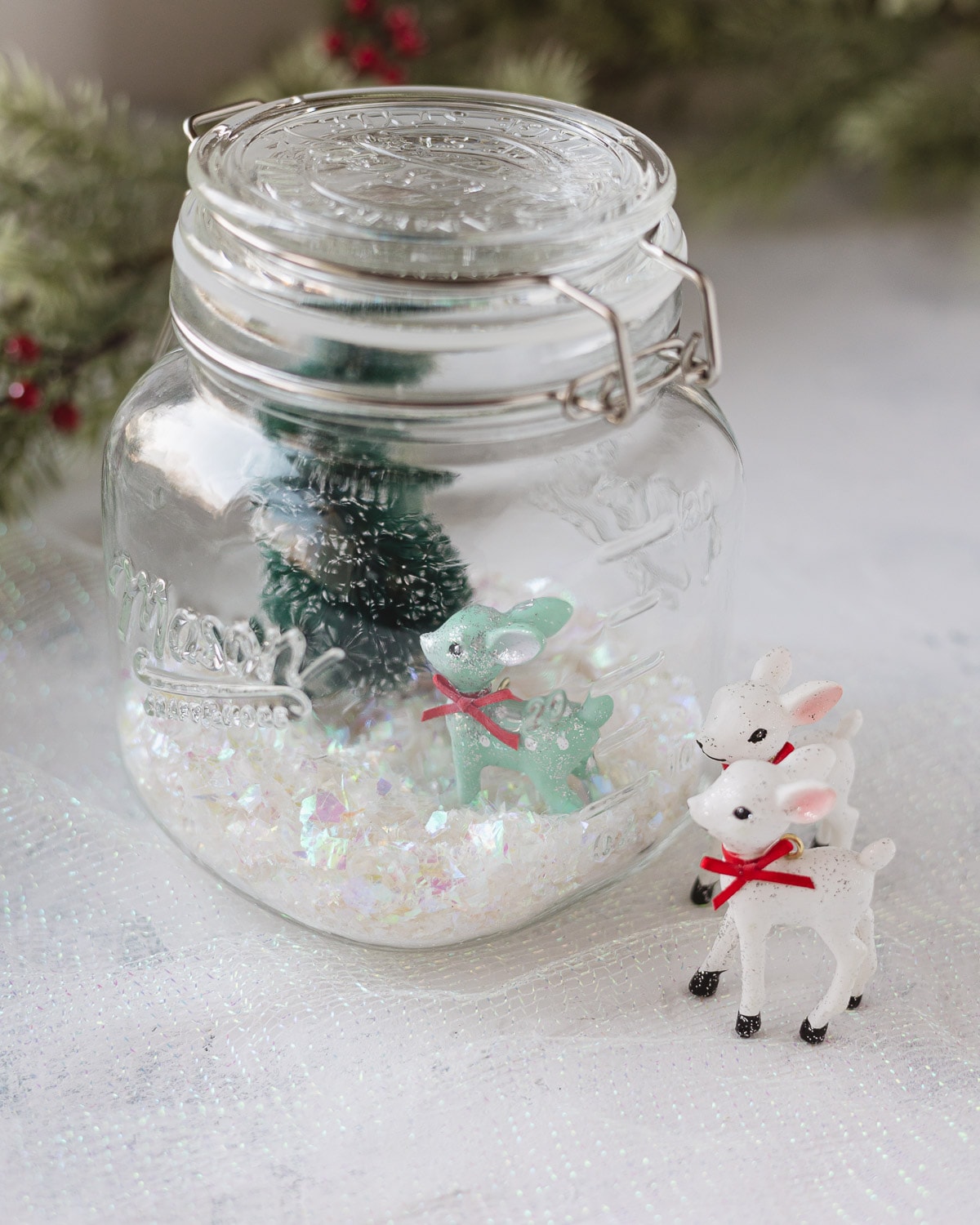 Two mini white reindeer and a mason jar filled with faux snow and a mini green reindeer.